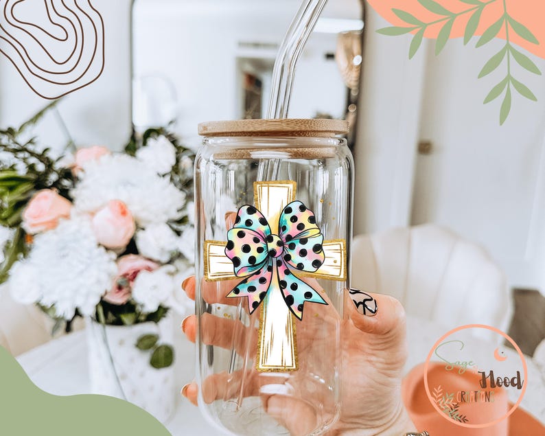 May include: A clear glass tumbler with a bamboo lid and a straw. The tumbler has a colorful bow and cross design on it.