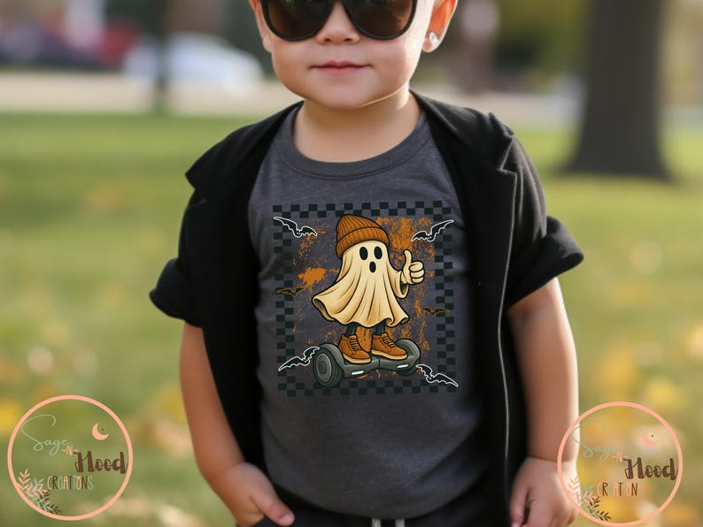 May include: A dark grey t-shirt with a cartoon ghost wearing a beanie and trainers, riding a hoverboard. The ghost gives a thumbs-up. The design includes bats and a checkered background, ideal for Halloween.
