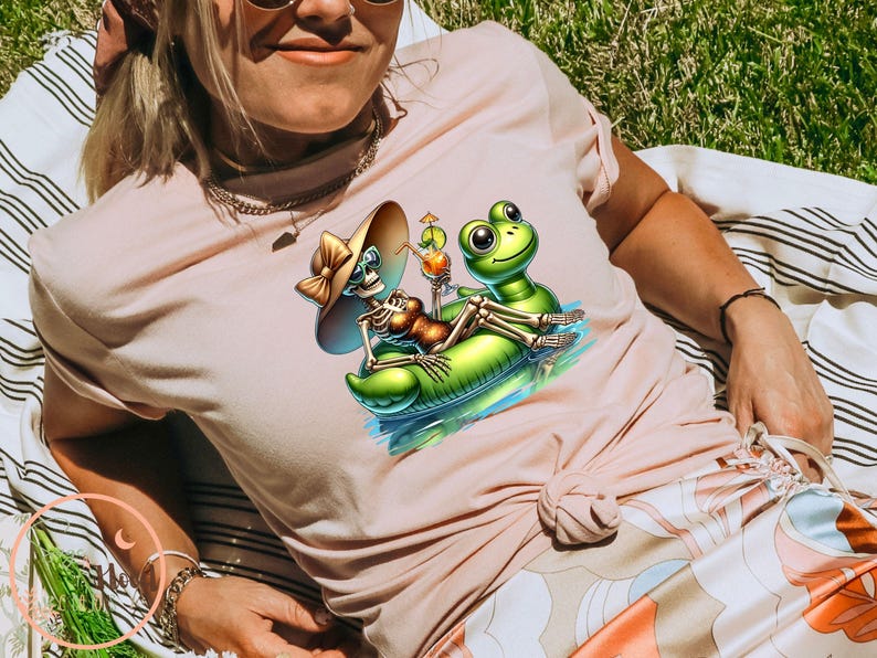 Może przedstawiać: R&oacute;żowy t-shirt z grafiką szkieletu w kapeluszu przeciwsłonecznym, jadącego na nadmuchiwanej zielonej żabie z koktajlem. Żaba ma na sobie zielony kapelusz.