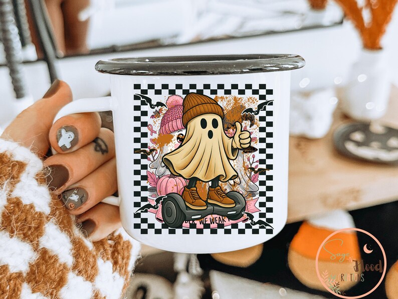 May include: White enamel mug with a black rim. The mug features a cartoon ghost on a hoverboard, giving a thumbs up. The design includes a checkerboard background, bats, pumpkins, and the text "WE WEAK".