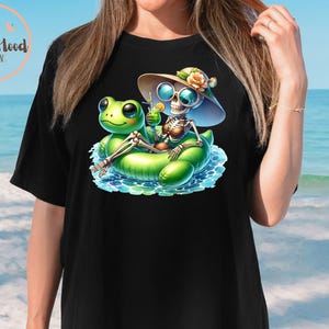 Może przedstawiać: Czarny T-shirt z grafiką przedstawiającą szkielet w kapeluszu przeciwsłonecznym i okularach przeciwsłonecznych, pływający na zielonej dmuchanej żabie. Szkielet trzyma zielony koktajl.