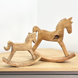May include: Two wooden rocking horses, one larger than the other, are arranged together. The larger horse is brown and has a natural wood finish. The smaller horse is also brown and has a natural wood finish. Both horses have a simple design and are made of solid wood.