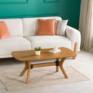 Peut inclure: Scène de salon avec un canapé blanc orné de coussins orange et à motifs. Une table basse en bois, avec une plante et une tasse, repose sur un tapis beige. La pièce présente un mur turquoise et une fenêtre avec un rideau blanc.