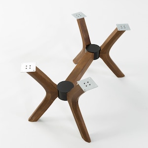 Pode incluir: Dois conjuntos de pernas de mesa de madeira com um design moderno de meados do século. As pernas são de cor castanho quente, com uma forma curva e suportes de metal preto. Cada perna tem uma placa de metal quadrada para fixar à mesa.