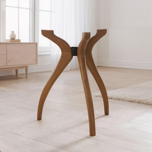 May include: A wooden table base featuring four curved legs that extend outward from a central black circular connector. The legs are finished in a medium brown wood tone and are positioned to support a tabletop that is not currently attached.