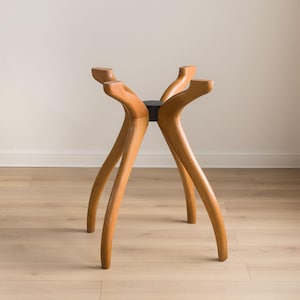 May include: A wooden table base with four curved legs and a black center support. The legs are a light brown color and have a smooth finish. The base is designed to support a tabletop and is suitable for a dining or coffee table.