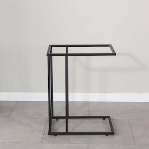 May include: A black metal side table with a rectangular top and a C-shaped base. The table is approximately 24 inches long, 12 inches wide, and 24 inches high. The design is minimalist and modern, suitable for various decor styles.