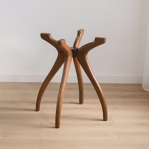 May include: A wooden table base with six curved legs. The legs are a warm brown color and meet at a central black support. The legs are evenly spaced and have a unique, organic shape. The table base is designed to support a tabletop.