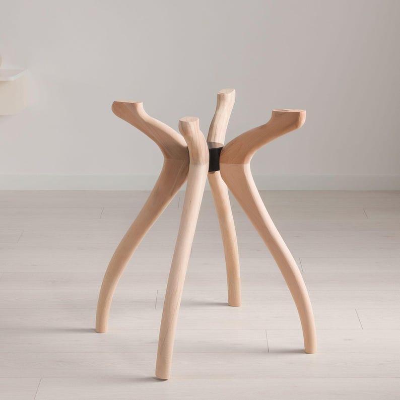 May include: A light-colored wooden stool with six curved legs. The legs are joined at the center with a black band. The stool's design is modern and minimalist, with a focus on natural materials and organic shapes. The stool is suitable for indoor use.