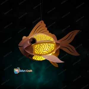 May include: A papercraft fish lantern with a light inside. The fish is orange and yellow with a white eye. The lantern is hanging from a string.