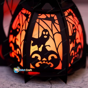 May include: A black paper lantern shaped like a pumpkin with a glow-in-the-dark design. The lantern features a ghost, spiderwebs, and a pumpkin face. The lantern is lit from inside, creating a warm orange glow.