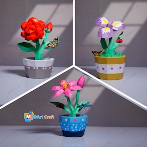 Puede incluir: Tres arreglos florales de papel en macetas. El primero presenta una rosa roja, el segundo iris moradas y el tercero un lirio rosa. Cada maceta tiene un diseño único y se incluyen pequeños insectos de papel.