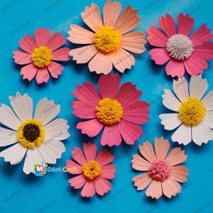 May include: A collection of handmade paper flowers in various shades of pink, peach, and white, with yellow or textured centers. The flowers are arranged on a bright blue background, showcasing the delicate petal details and craftsmanship. The text "M3DArt Craft" is visible.