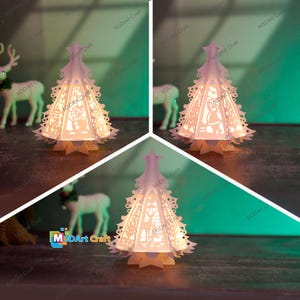 Könnte beinhalten: Ein weißer Papier-Weihnachtsbaum mit filigranen Ausschnitten und einem warmen Schein von einem Licht im Inneren. Der Baum steht auf einem Tisch mit grünem Hintergrund.
