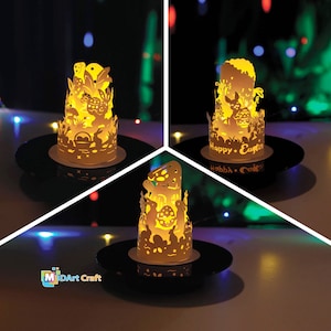 May include: Three illuminated papercraft Easter candle holders with intricate designs featuring bunnies, eggs, and other Easter motifs. The candle holders are on black circular bases and have the text "Happy Easter" on one of the bases.