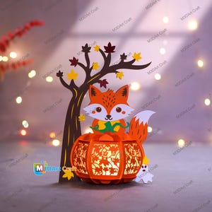 Peut inclure: Scène d'automne en papier avec un renard, un arbre et une lanterne citrouille. Le renard orange est assis sur la citrouille, avec un arbre brun et des feuilles colorées. Un petit fantôme blanc est à côté de la citrouille. La lanterne brille d'une lumière chaude.