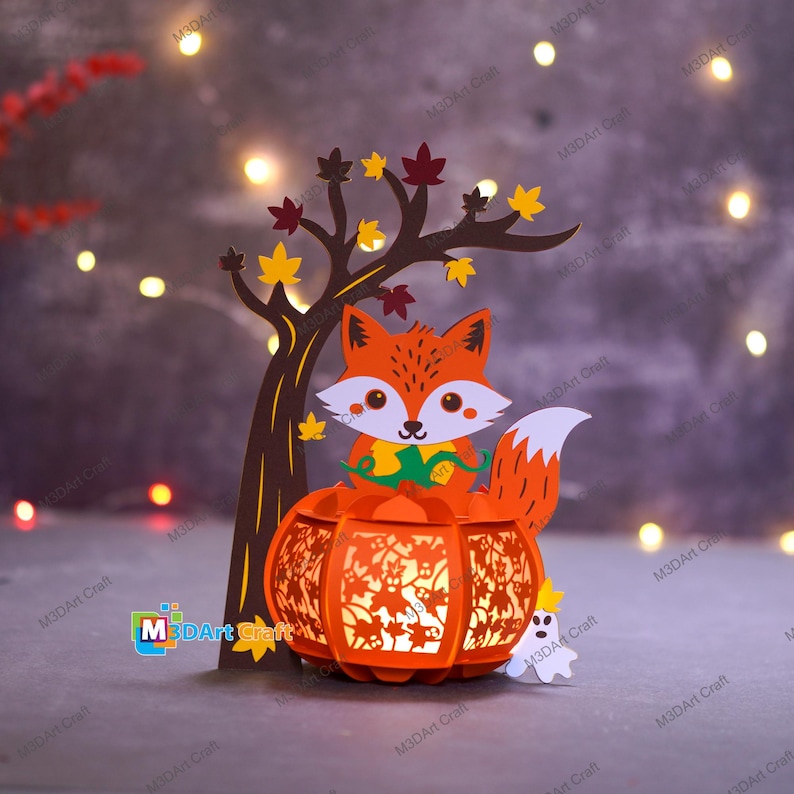 May include: A papercraft autumn scene featuring a fox, a tree, and a pumpkin lantern. The orange fox has a white face and tail, and sits atop a carved pumpkin. The tree has brown bark and colorful leaves. A small white ghost is also present.