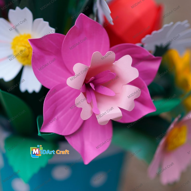 May include: Close-up of a vibrant paper flower arrangement. The focal point is a large, magenta-colored flower with a lighter pink center. Other flowers include white daisies with yellow centers and a red flower. The arrangement is in a blue polka-dotted container.