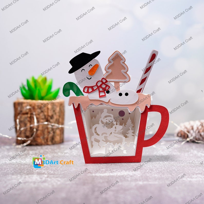 K&ouml;nnte beinhalten: Eine rote und wei&szlig;e Papiercraft-Tasse mit einem Schneemann, einem Zuckerstangen und einem kleinen Weihnachtsbaum oben drauf. Die Tasse ist mit einem wei&szlig;en Schneeflockenmuster und einem roten Griff verziert.