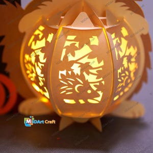 May include: A paper lantern in the shape of a hedgehog, with intricate cut-out designs. The lantern is illuminated from within, casting a warm, inviting glow. The design includes leaves and a hedgehog silhouette. The product is from M3DArt Craft.