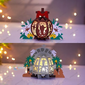 May include: Two layered paper art pieces. The top piece is a brown sphere with a cutout of a religious figure, a cross, and red fabric. The bottom piece is a white structure with a cutout of a religious figure and palm trees. White and yellow flowers are in the foreground.