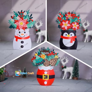Peut inclure: Trois décorations de Noël en papier. Un bonhomme de neige avec une écharpe rouge, un pingouin avec une écharpe rouge et un Père Noël. Chaque décoration contient un bouquet de fleurs et de verdure en papier coloré.