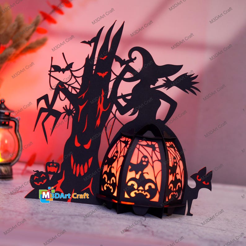 May include: A black and orange Halloween-themed papercraft lamp with a witch, a tree, bats, and pumpkins. The lamp is lit and glows orange.