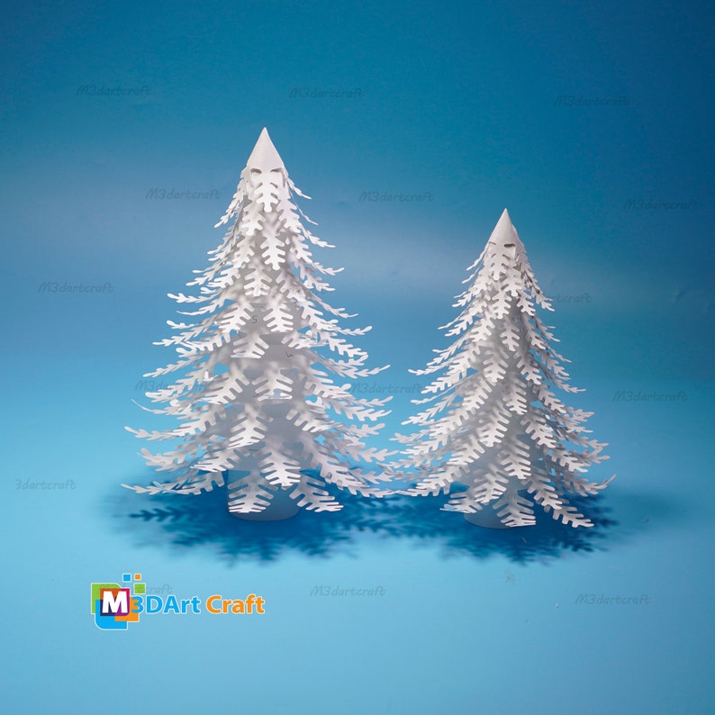 Peut inclure: Deux sapins de No&euml;l en papier blanc sur un fond bleu. Le plus grand sapin est au centre de l'image et le plus petit est &agrave; droite. Les sapins sont en papier et ont un effet 3D. Le texte "M3DArt Craft" est en bas de l'image.