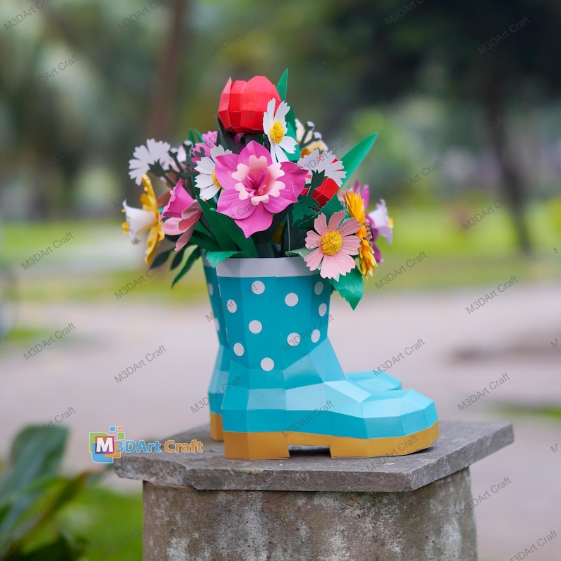 May include: A paper flower arrangement in a turquoise polka-dot rain boot. The boot has a yellow sole and holds a variety of colorful paper flowers, including pink, red, white, and yellow blooms. The arrangement is displayed on a stone surface.