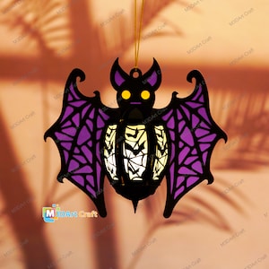 May include: A black and purple bat-shaped paper lantern with a white and black spiderweb design. The lantern has a yellow light inside and is hanging from a string.