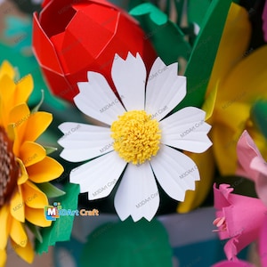 May include: A close-up of a paper flower arrangement featuring a large white daisy with a yellow center, a red tulip, and a yellow sunflower. The arrangement is colorful and detailed, with visible papercrafting techniques.