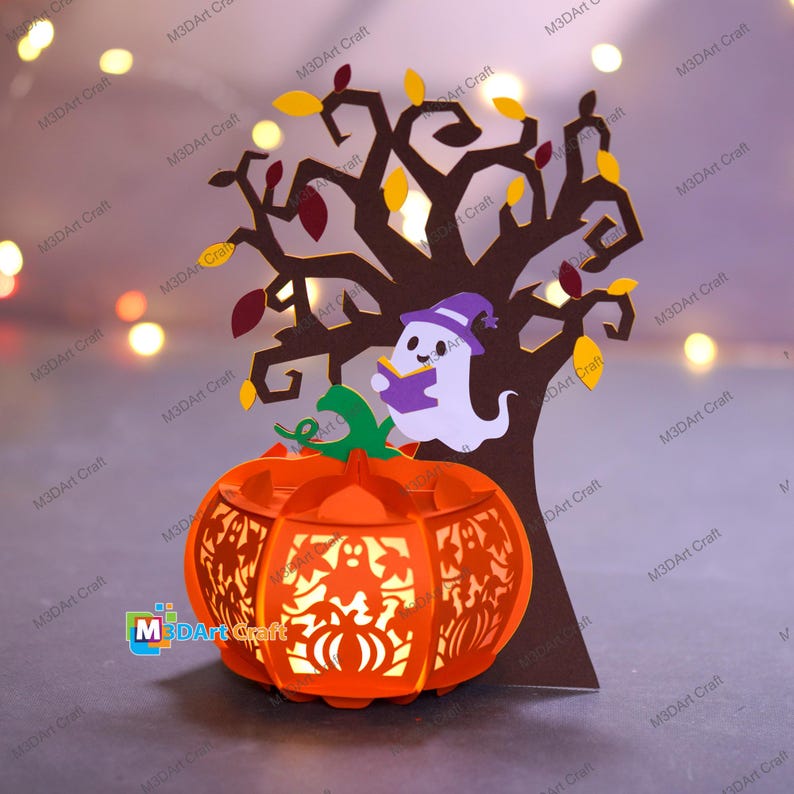 May include: A papercraft Halloween decoration featuring a glowing orange pumpkin lantern with cut-out designs. A brown tree with colorful leaves and a friendly ghost reading a book are behind the pumpkin. The text "M3DArt Craft" is visible.