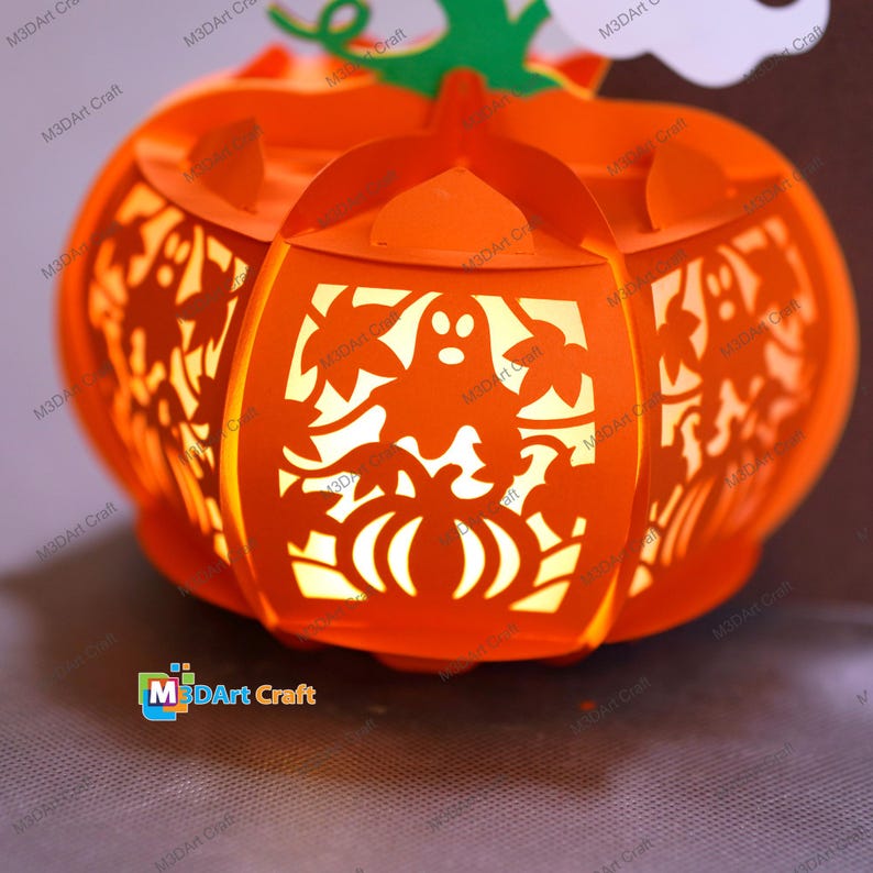 May include: An orange paper lantern shaped like a pumpkin, with cut-out designs of ghosts, leaves, and pumpkins. The lantern is lit from within, creating a warm glow. A green stem and white cloud accent the top. Perfect for Halloween.