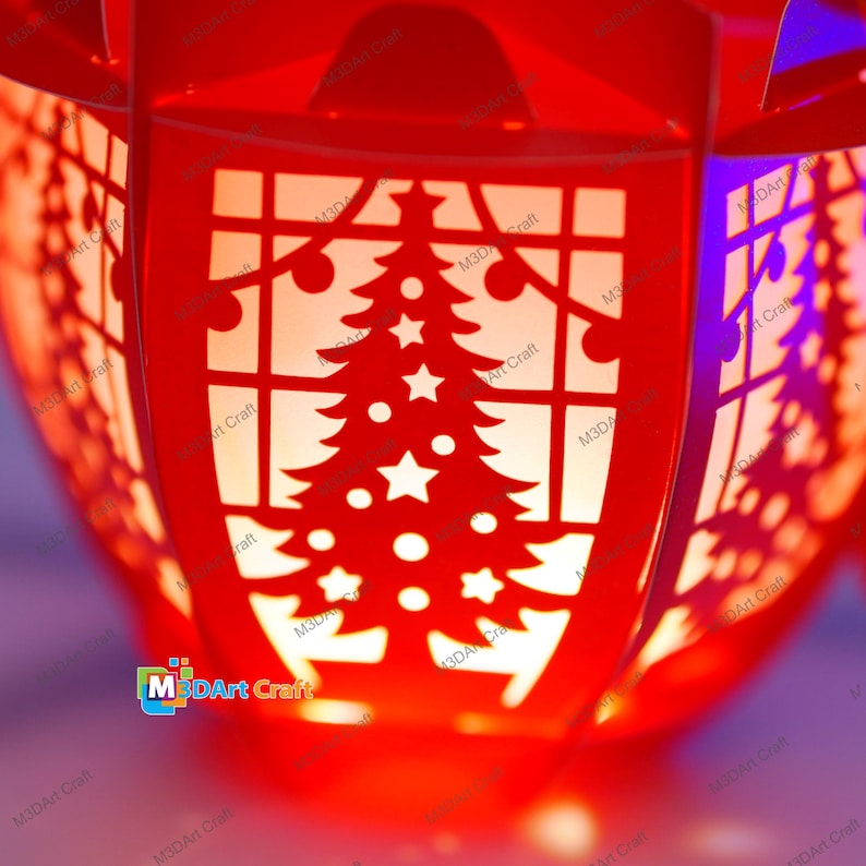 Puede incluir: Linterna roja de Navidad con un dise&ntilde;o recortado de un &aacute;rbol de Navidad y estrellas. La linterna est&aacute; iluminada desde adentro, creando un brillo c&aacute;lido.