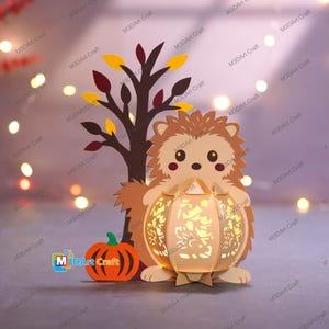 May include: A papercraft autumn scene featuring a hedgehog holding a glowing lantern. A small orange pumpkin and a brown tree with yellow and red leaves are also present. The text "M3DArt Craft" is visible.