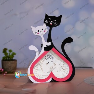 May include: A white and black papercraft of two cats in a heart-shaped frame. The cats are holding each other and the frame says "My Love".