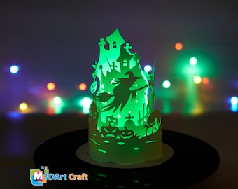 May include: A green papercraft Halloween lantern with a witch, a haunted house, pumpkins, and a cat. The lantern is lit from within, casting a warm glow.