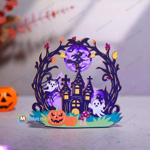 以下が含まれることがあります： ハロウィーンをテーマにした多層構造の装飾品。濃い紫色の幽霊屋敷、2体の白い幽霊、オレンジ色のカボチャ、魔女のシルエットが描かれた紫色の月が特徴で、小さな黄色い葉がついた濃い紫色の木の枝で縁取られています。