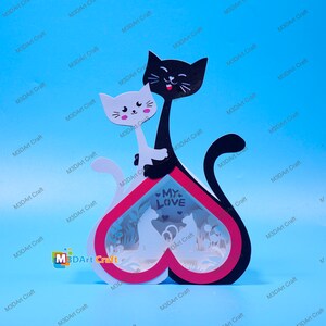 May include: A white and black cat couple figurine with a heart-shaped base. The base is red with a white interior and features a cutout design of a cat couple. The base has the words "My Love" written on it.