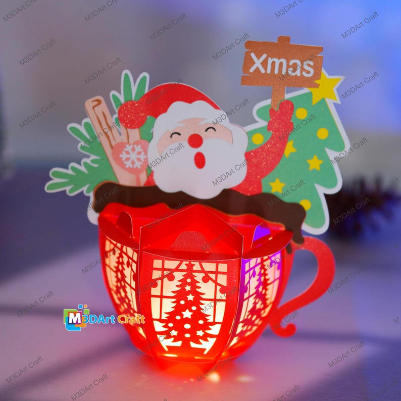 Puede incluir: Una taza de papel roja con un dise&ntilde;o de Pap&aacute; Noel y un &aacute;rbol de Navidad. La taza est&aacute; iluminada desde adentro, creando un brillo c&aacute;lido. El letrero sobre la taza dice "Xmas".