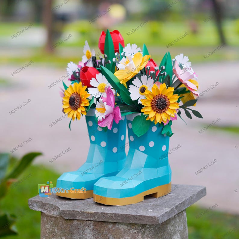 May include: A pair of light blue paper boots with white polka dots, holding a colorful bouquet of paper flowers. The flowers include sunflowers, daisies, and tulips. The boots have yellow soles and are displayed on a stone surface.