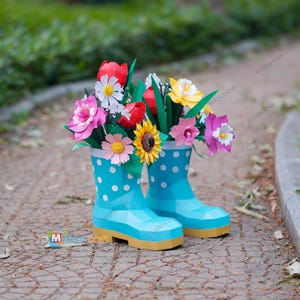 May include: A pair of light blue paper boots with white polka dots, filled with colorful paper flowers. The flowers include red tulips, yellow sunflowers, pink and white daisies, and other blooms. The boots have a yellow sole.