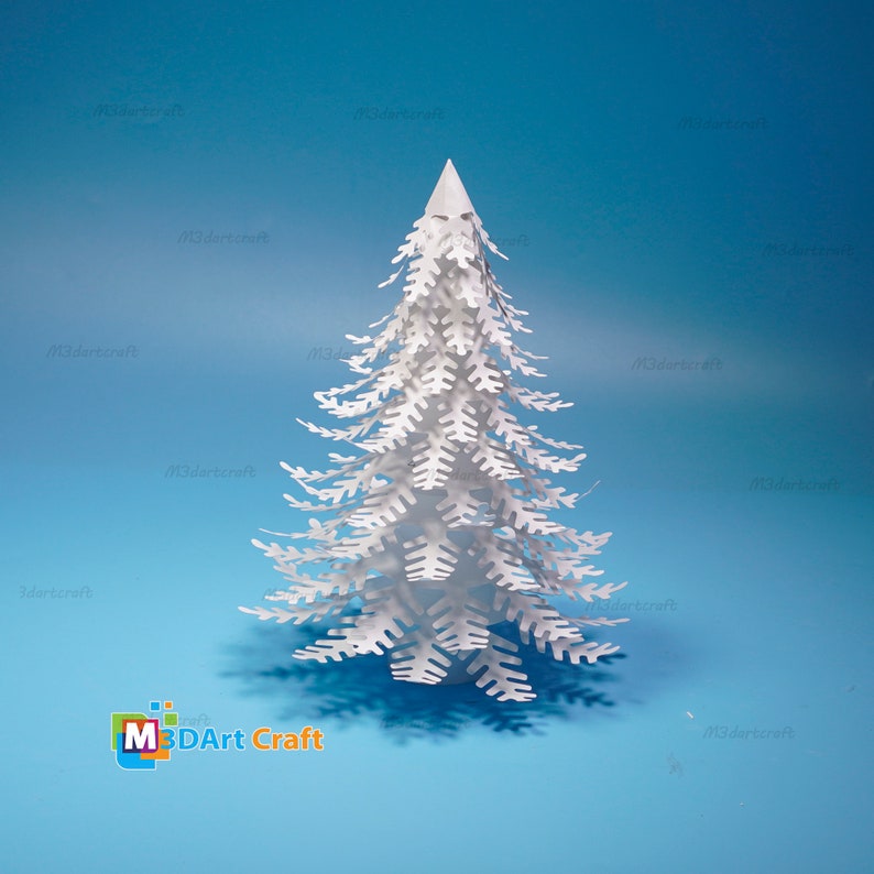 Peut inclure: Un arbre de No&euml;l en papier blanc avec des d&eacute;tails complexes, sur un fond bleu clair. L'arbre est fait de papier en couches et a un effet 3D. L'image comprend le texte "M3DArt Craft".