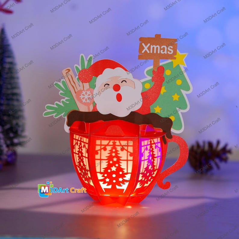 Puede incluir: Una linterna de papel roja con forma de taza con un dise&ntilde;o de Pap&aacute; Noel y un &aacute;rbol de Navidad. La linterna tiene una luz en el interior y dice "Xmas" en un cartel.