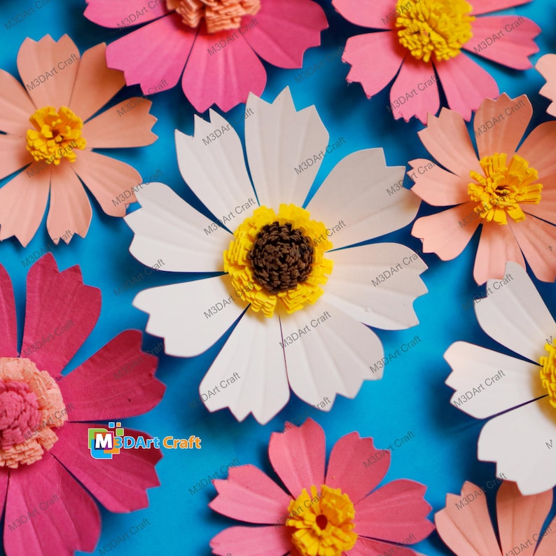 May include: A collection of handmade paper cosmos flowers in shades of pink, peach, and white, with yellow and brown centers. The flowers are arranged on a bright blue background. The text "M3DArt Craft" is visible on some of the flowers.