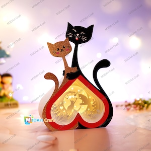 Könnte beinhalten: Eine 3D-Papier-Herzlampe mit einer schwarzen Katze und einer braunen Katze im Inneren. Die Katzen halten ein Herz und die Lampe hat ein rotes und weißes Herzdesign.