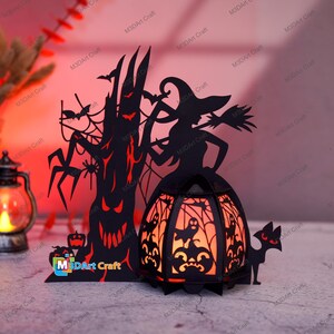May include: A black papercraft Halloween scene with a witch, a spooky tree, a cat, and a lantern. The lantern is lit and glows orange. The scene is against a red background.