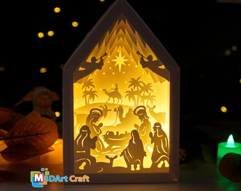 May include: A white wooden nativity scene with a light inside, depicting the birth of Jesus with Mary, Joseph, and the baby Jesus in a manger. The scene is illuminated from behind, creating a warm glow. There are palm trees and a star in the background.