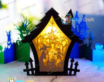 May include: A black papercraft Halloween scene with a lit-up house, a witch, a child, and a fence. The scene is illuminated from behind, creating a glowing effect.