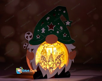 Pode incluir: Uma figura de gnomo de Natal de madeira com uma função de iluminação. O gnomo está usando um chapéu verde com estrelas brancas e uma estrela vermelha. O rosto do gnomo é branco com um nariz vermelho e uma barba branca. A função de iluminação é uma janela circular na barriga do gnomo que mostra uma cena de Natal com uma árvore, uma lareira e dois gnomos menores.